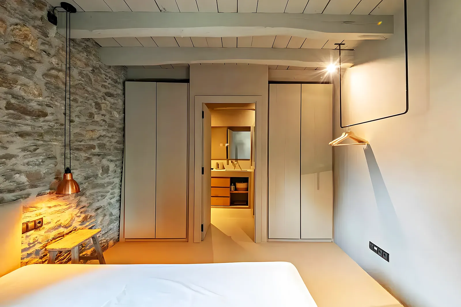 Dormitorio con muro de piedra vista recuperado en una casa de pueblo reformada en Sant Pere de Ribes