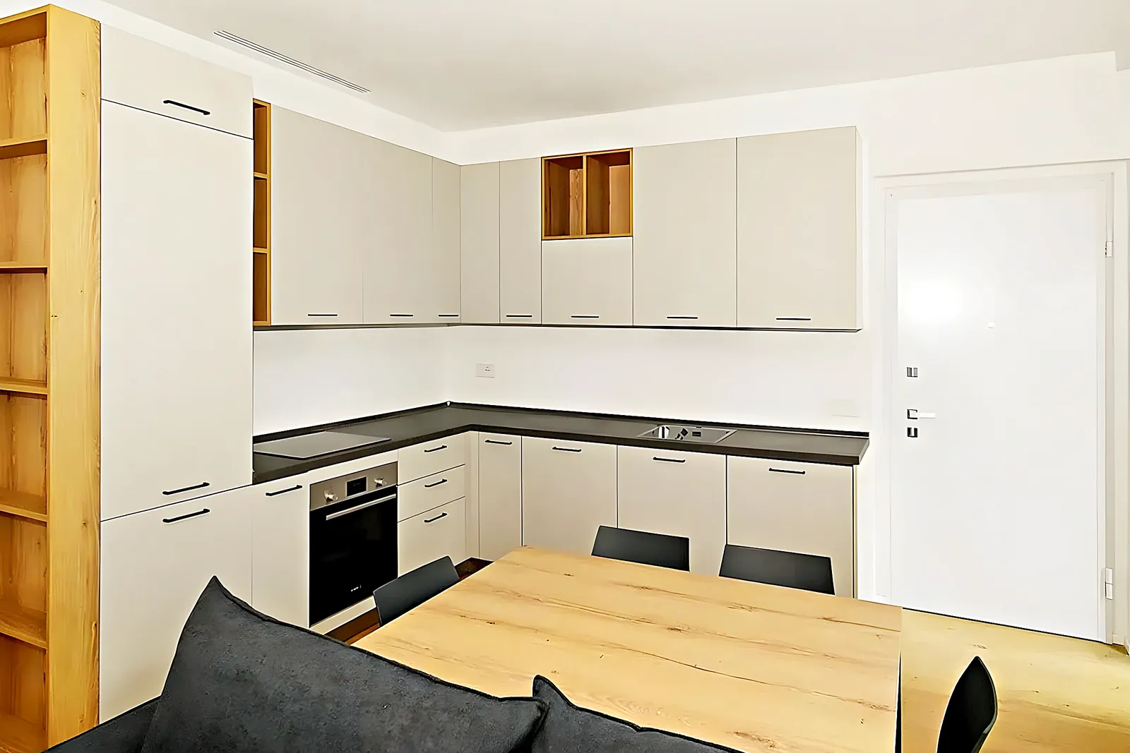 Cocina blanca abierta con mesa de comedor de madera en un piso reformado de Les Roquetes