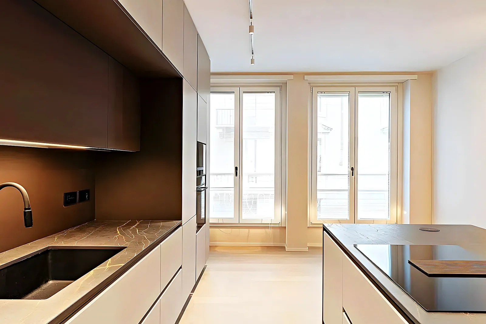 Cocina con isla y grandes ventanales de perfil dorado en una reforma en Vilanova i la Geltrú