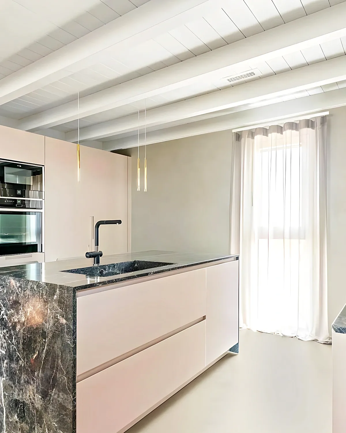 Cocina blanca con isla de mármol gris y techo de vigas en una casa del Aragai, Vilanova i la Geltrú