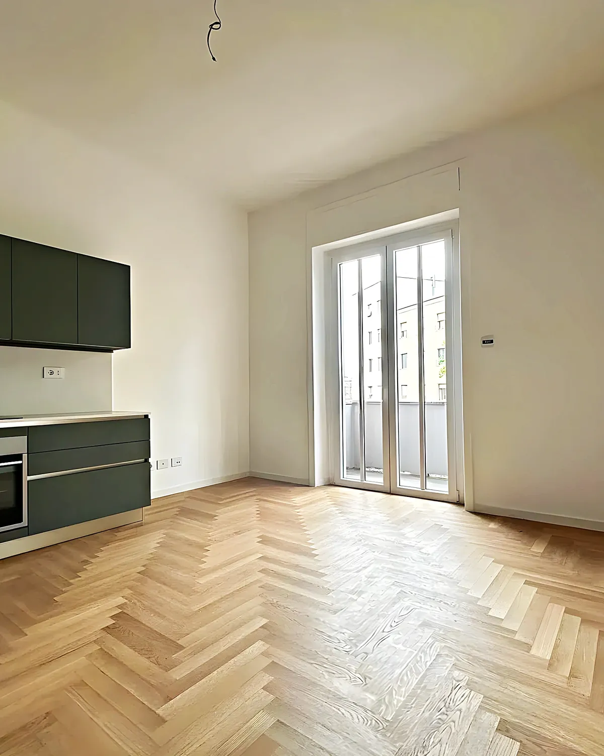 Cocina verde abierta con suelo de parquet en espiga en un piso reformado de Les Roquetes