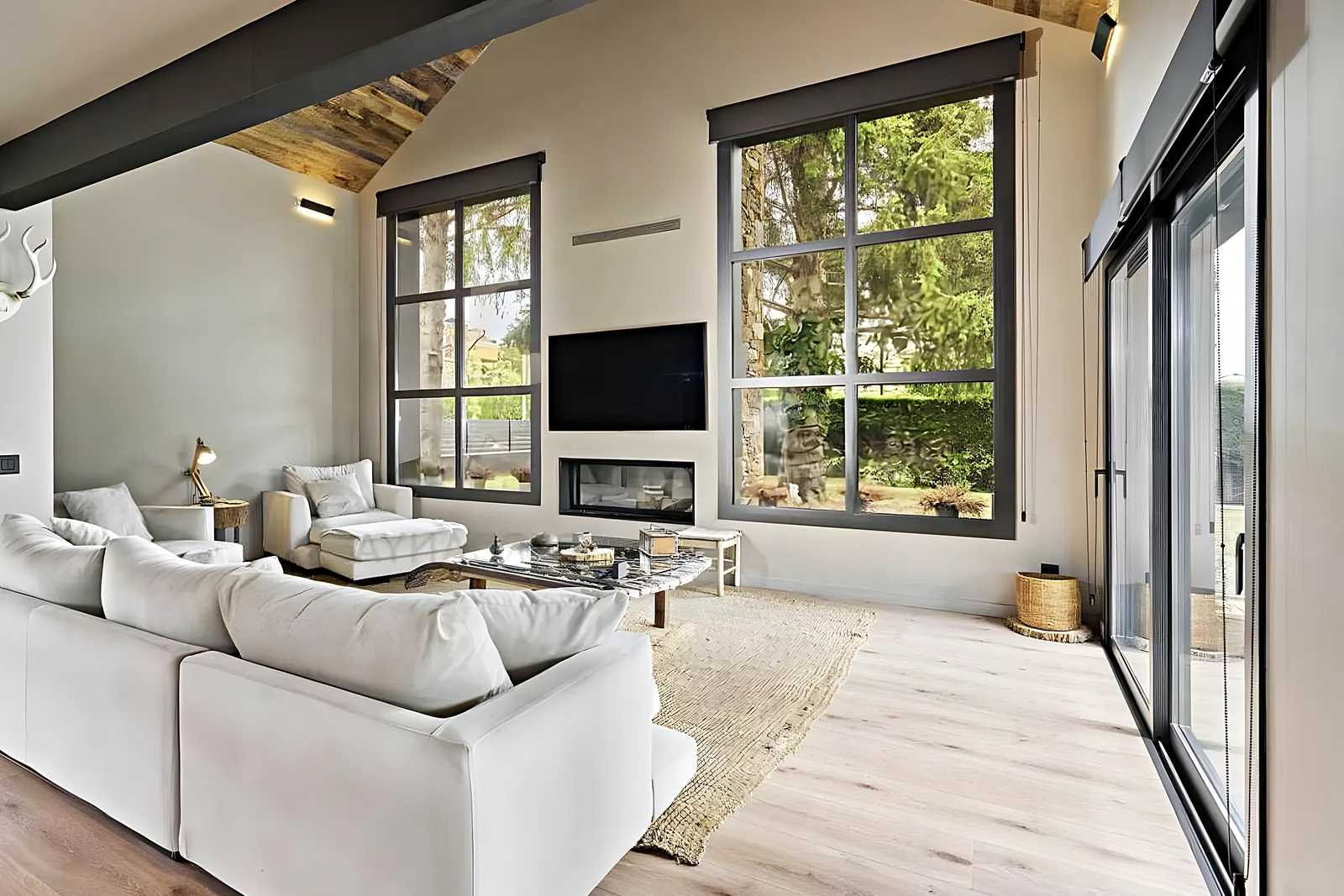 Salón reformado con ventanales de carpintería negra y chimenea, obra de Reformas Vilanoví